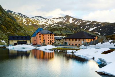 A high angle shot of some houses by a lake near the snow-covered mountains